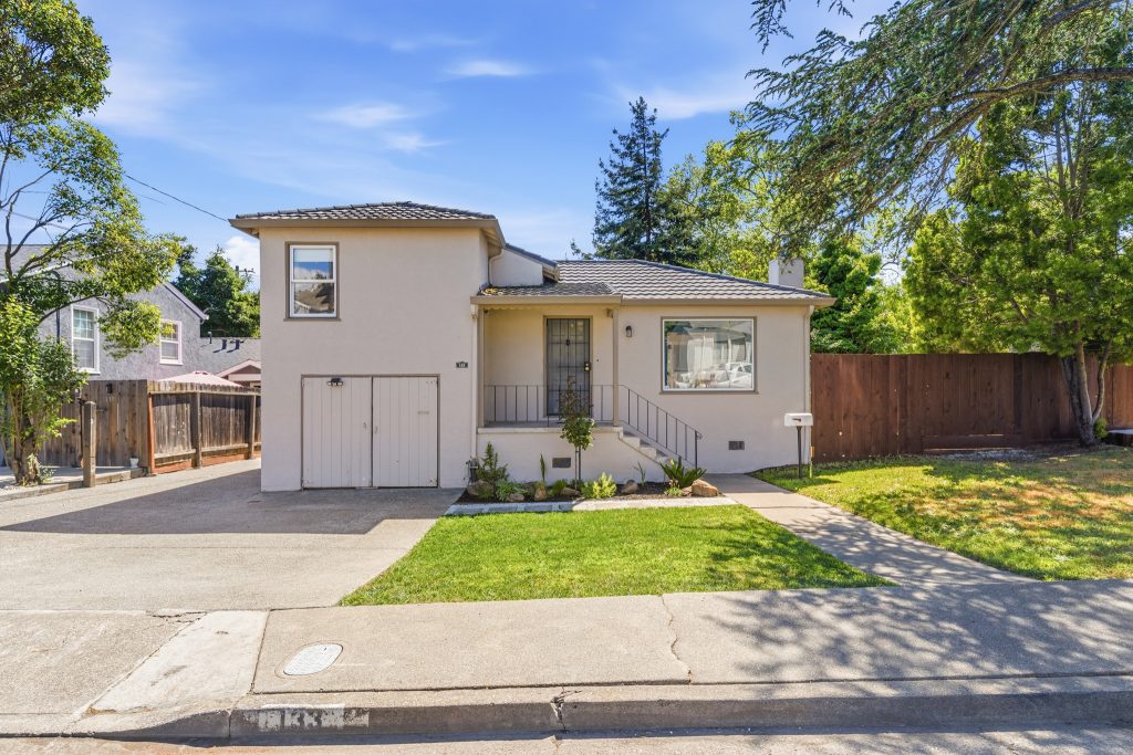 Front exterior of updated 133 Claremont Ave Vallejo home with stucco finish, attached garage, driveway parking, and landscaped front yard under mature trees